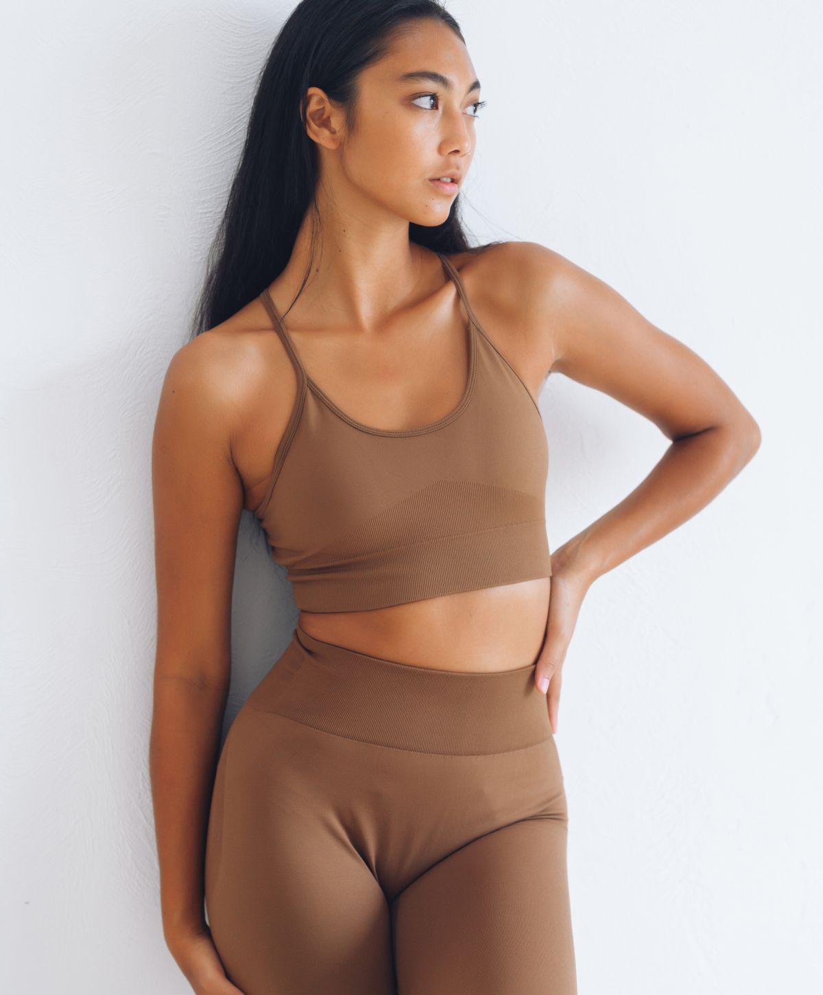 facial contouring patient model in brown sports bra and yoga pants standing against a wall with a hand on her waist