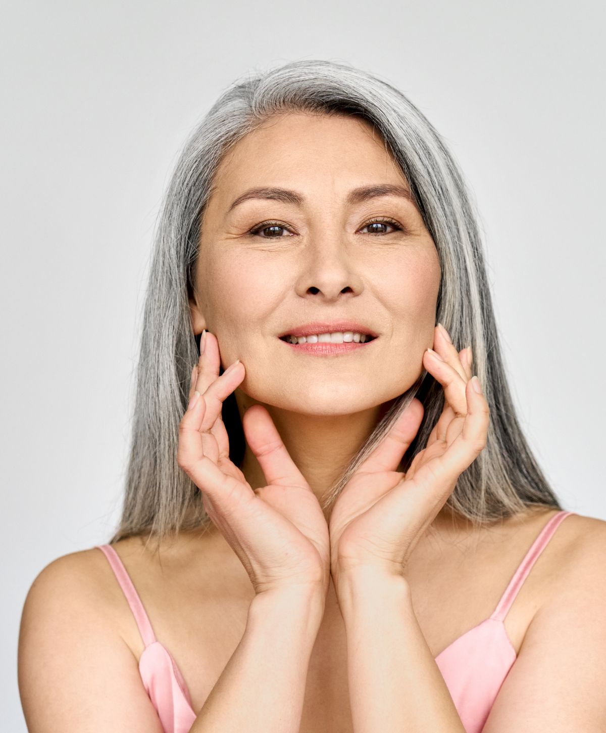 Smiling facial contouring patient model with long gray hair indoors.