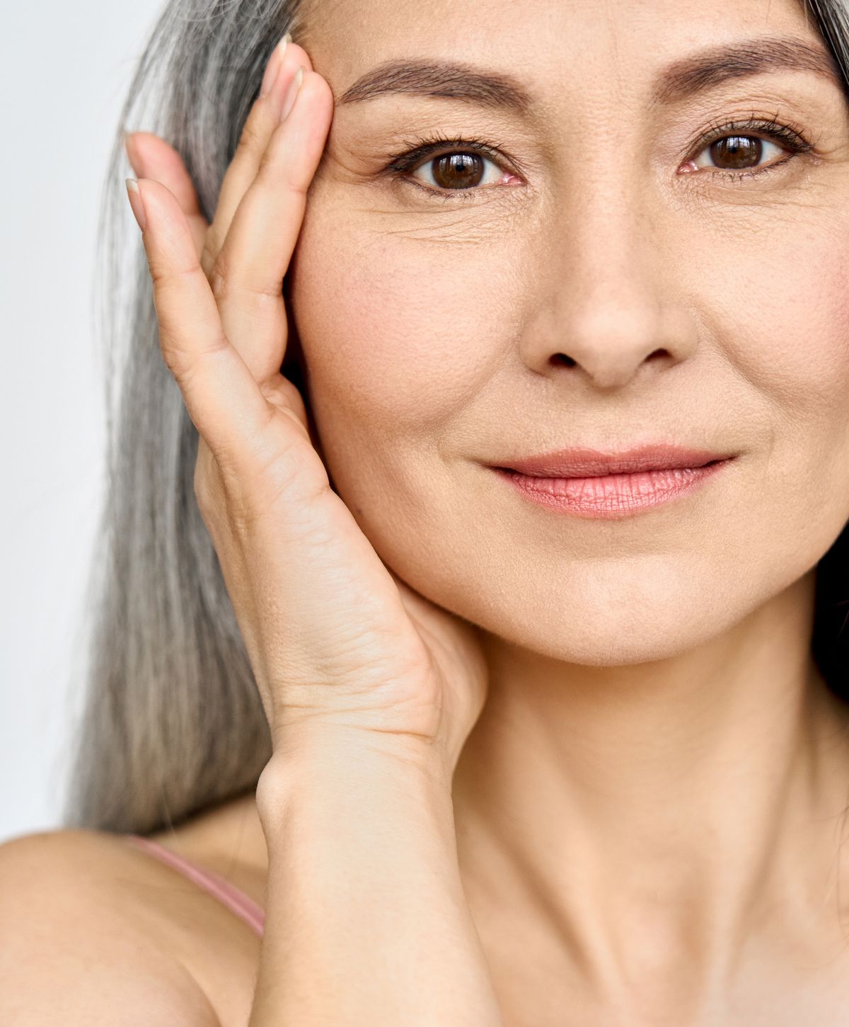Woman with gray hair gently touching her face.