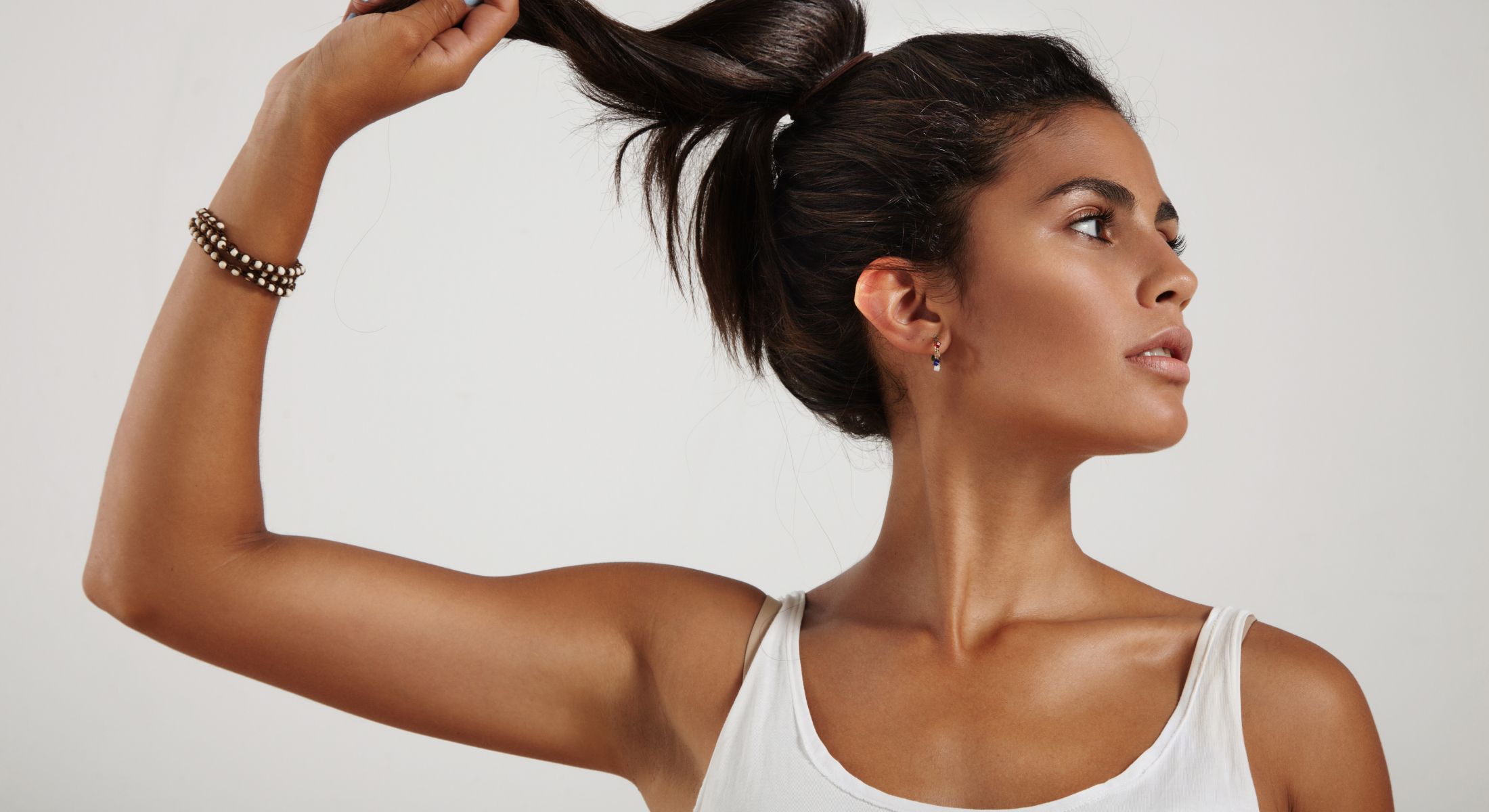 med spa patient model in a white tank top touching her ponytail